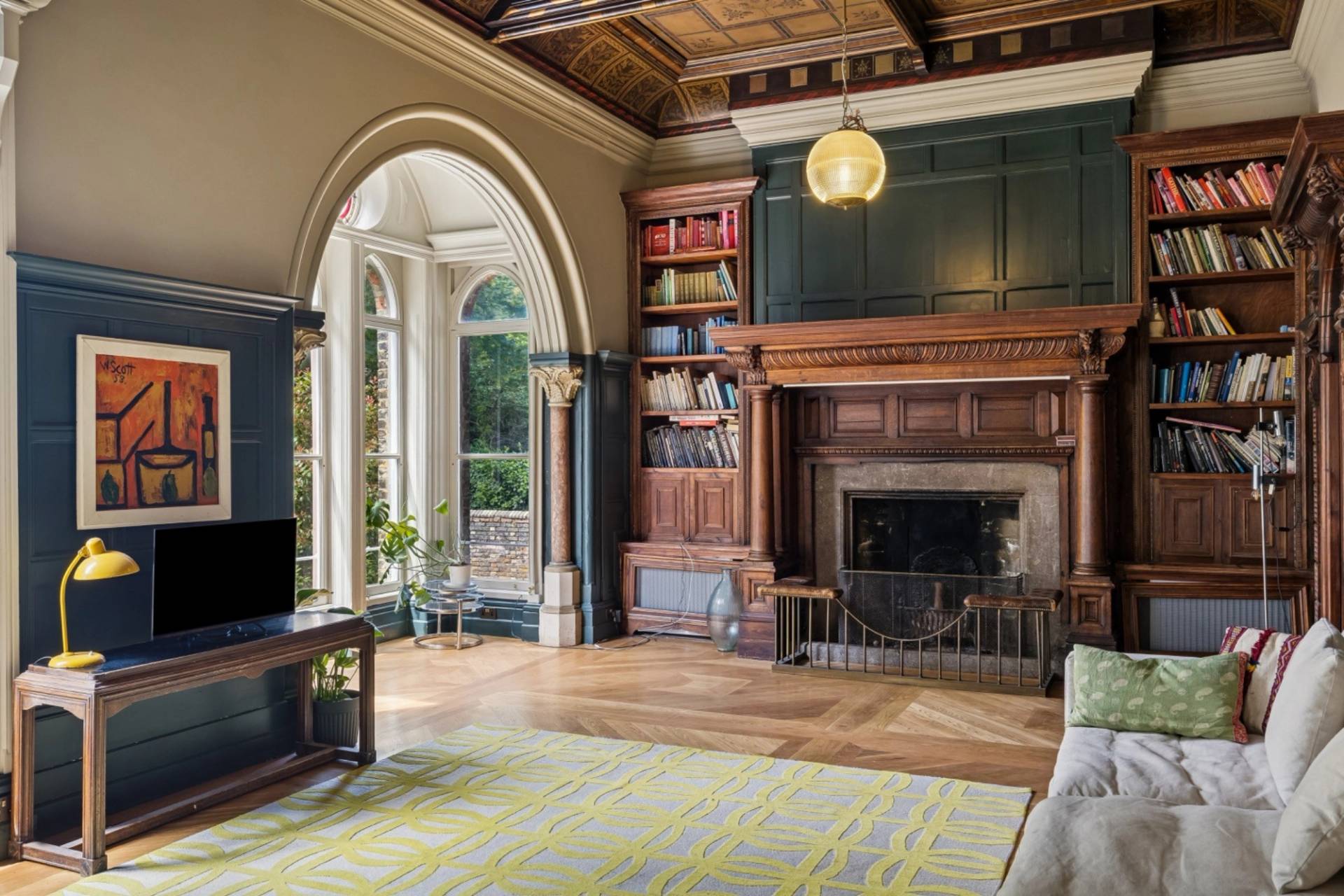 Period library room with carved wood fireplace and arched window in a gothic Hampstead home via Love Locations.