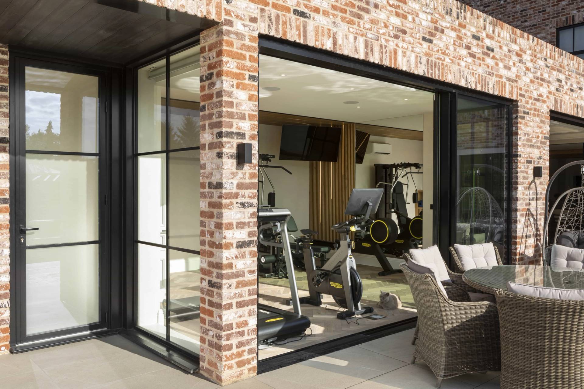 Private home gym set within a red brick pool house enclosure featuring glass sliding doors, Love Locations HP18.