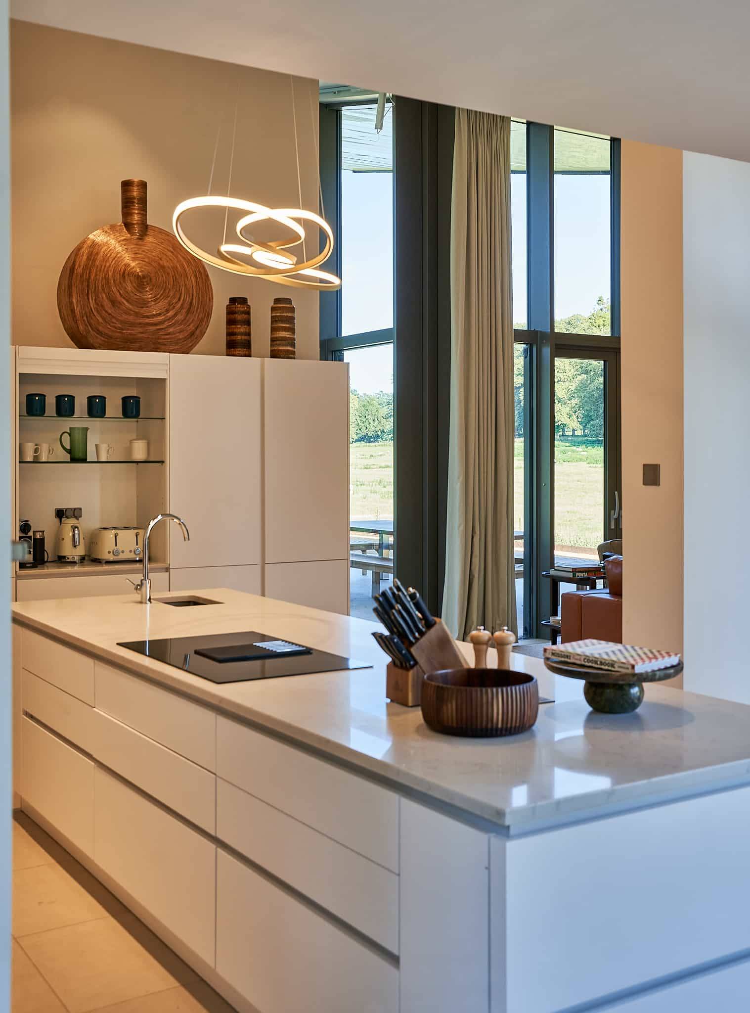 Sleek modern white kitchen island with marble countertops and floor-to-ceiling garden windows, Love Locations SO21.