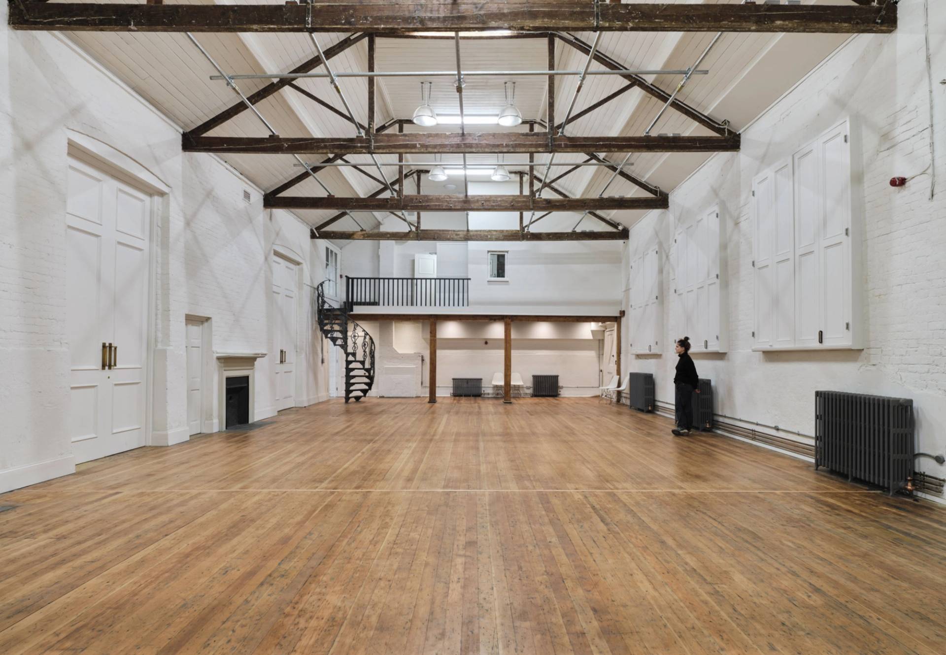Wide-angle perspective of an empty vaulted event hall with dark wooden floors and spiral staircase balcony access, perfect for pop-up exhibitions, Love Locations E2.