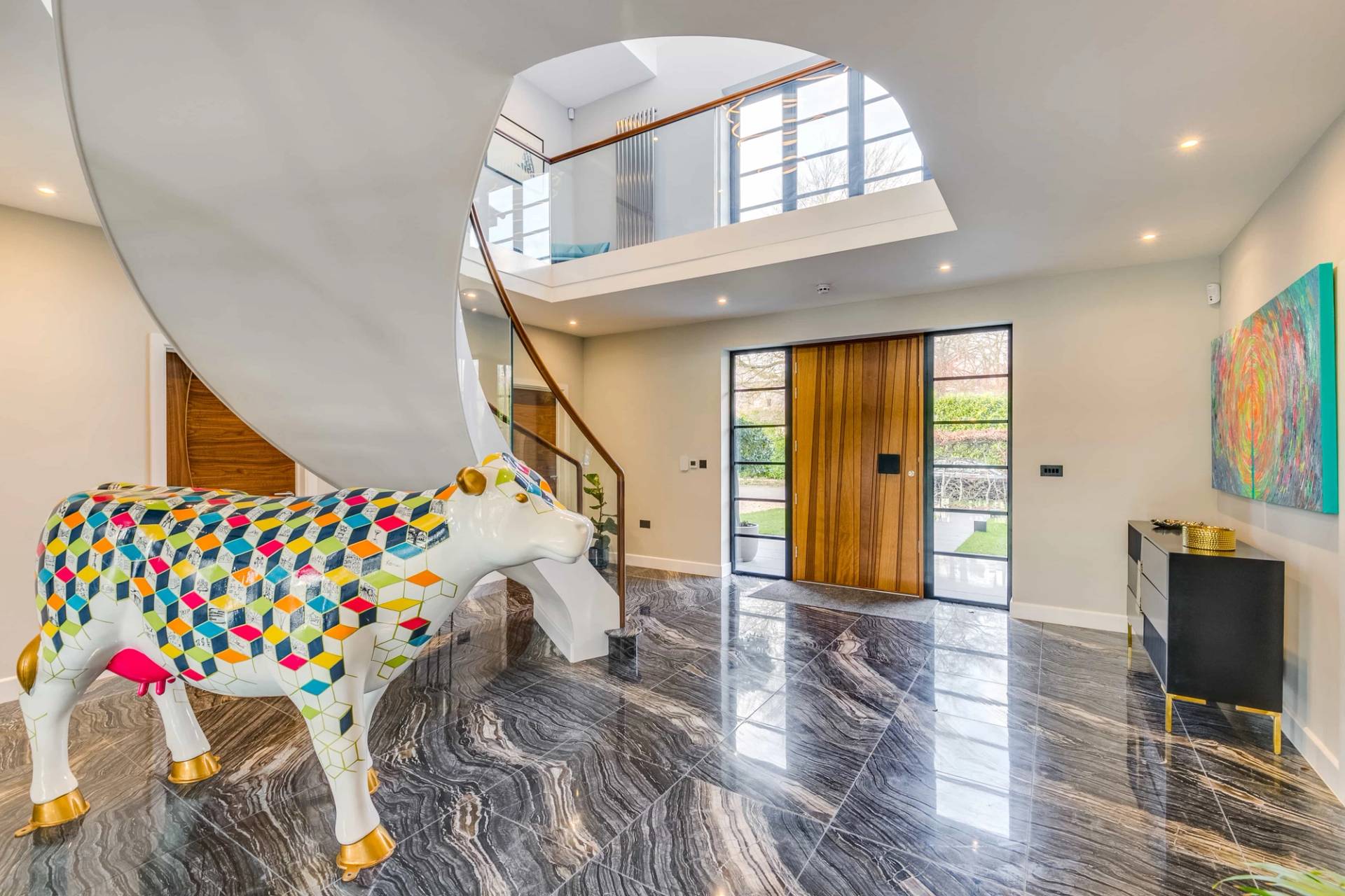 Entrance foyer detail showing a colorful painted cow statue beside a curved white staircase, Love Locations CB2.