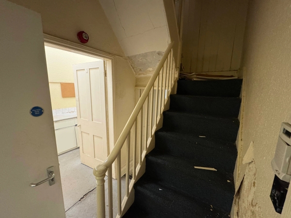 Narrow wooden service staircase inside a derelict mansion building leading up towards a plain white door, Love Locations.