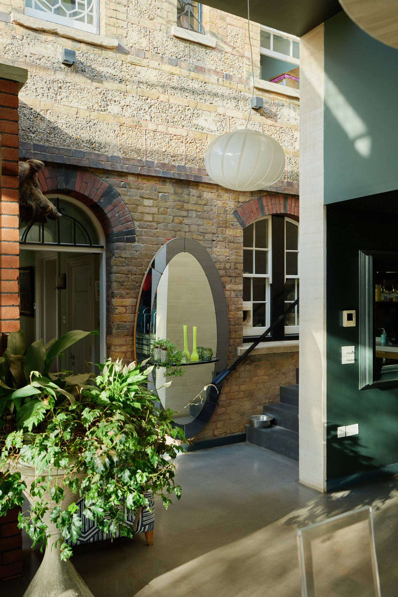 Internal hallway view showing exposed yellow brick walling, large oval wall mirror, and grey concrete floors in Wimbledon, Love Locations SW20.