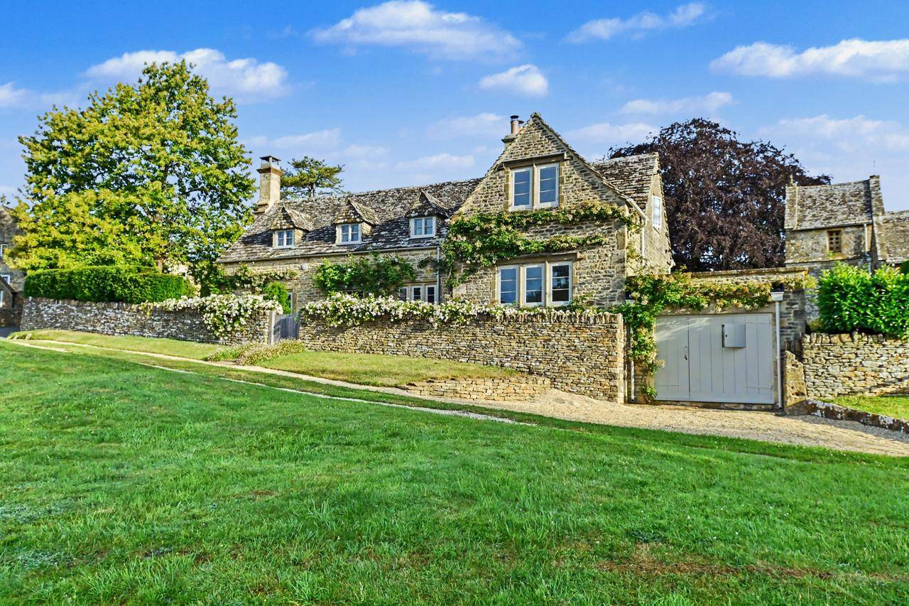 Picturesque Cotswold stone cottage facade photoshoot location in Gloucestershire GL7 through Love Locations, displaying climbing plants, stone chimneys, and manicured front lawns.
