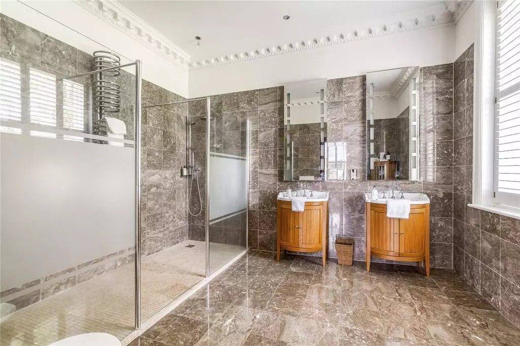Opulent marble-tiled master bathroom location house in Reading RG10 through Love Locations, featuring double wooden washbasin vanities and a glass walk-in shower.