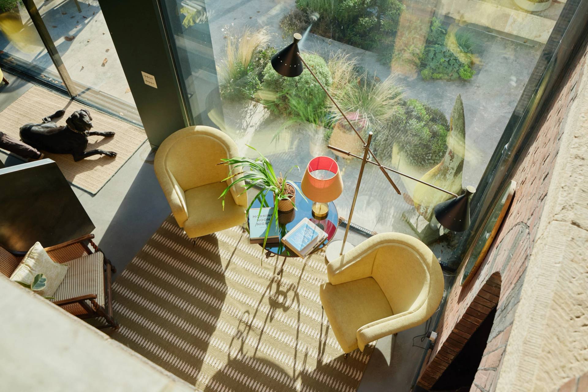 High-angle perspective of yellow velvet armchairs set on a striped rug beside glass lightwell windows, Love Locations SW20.