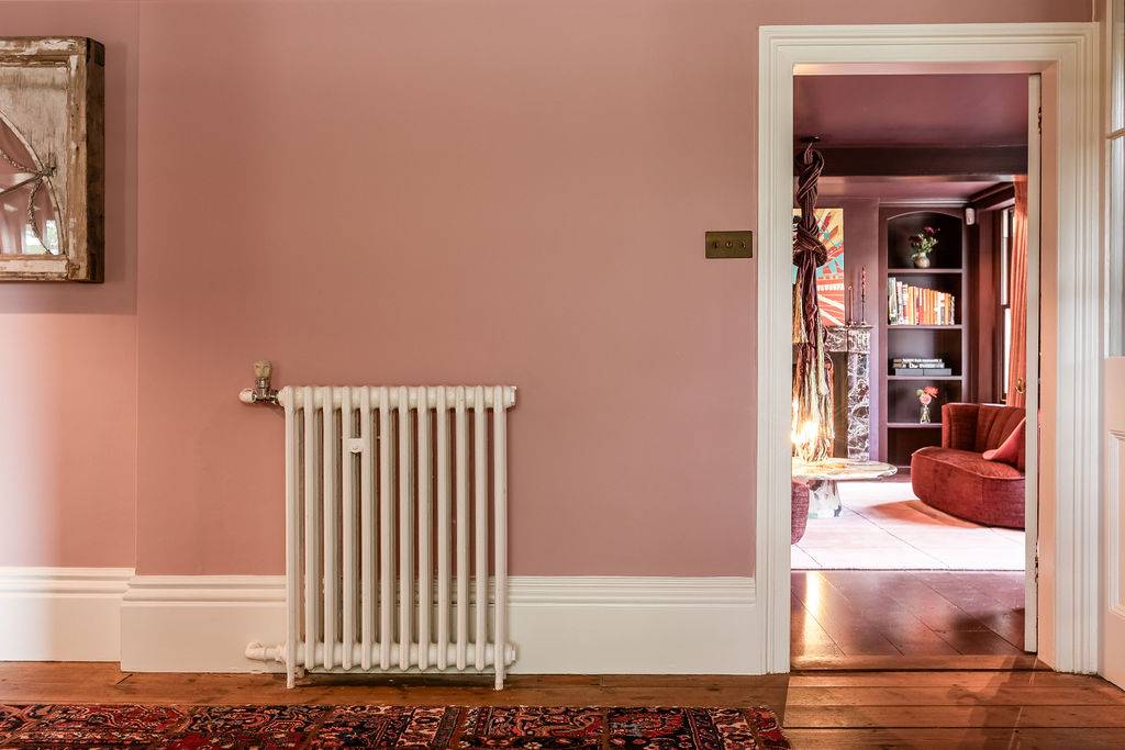 Traditional white cast-iron radiator set against a soft pink plaster partition wall inside a location home by Love Locations.