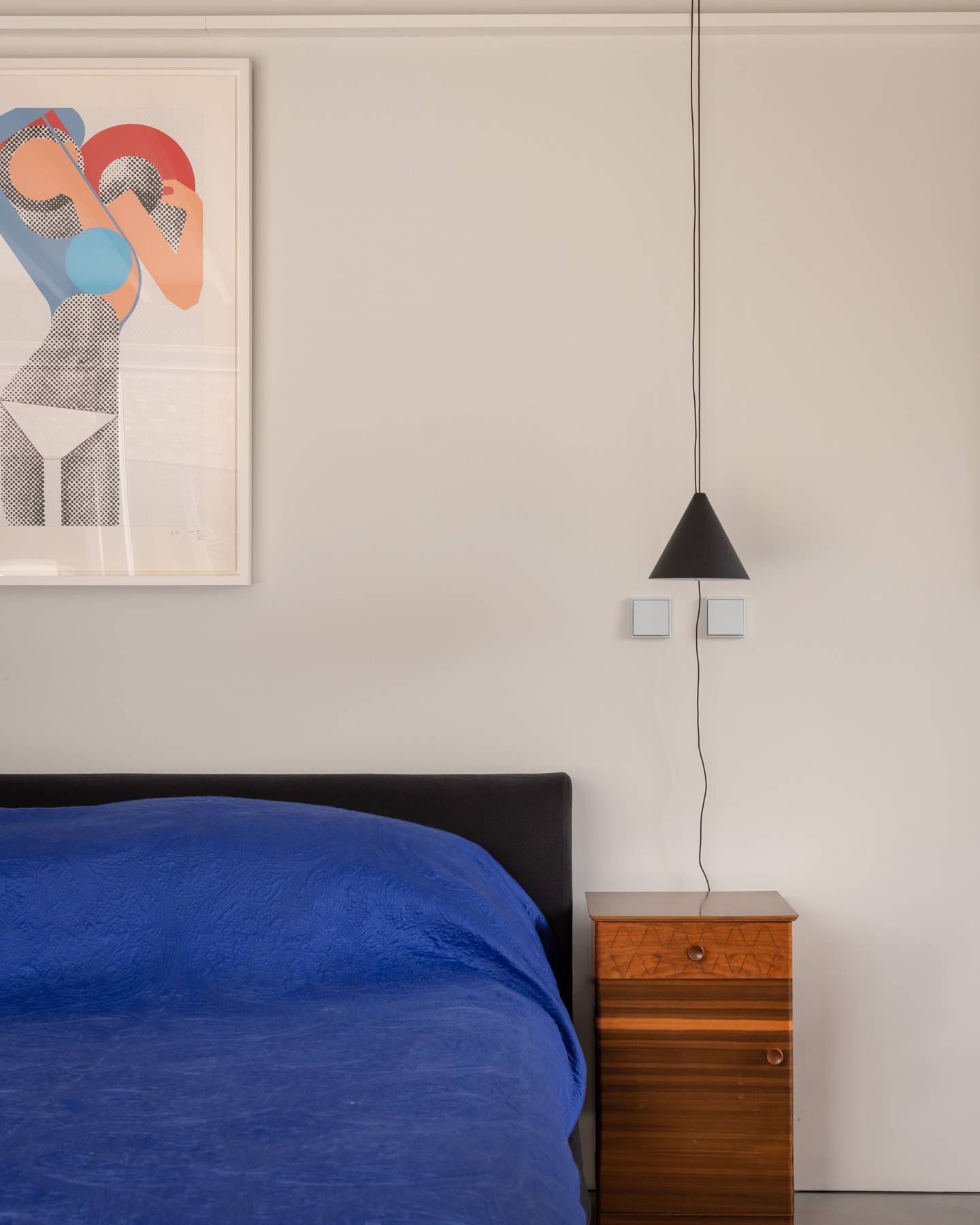 Minimalist bedroom detail featuring a vibrant blue bed against white walls with a black pendant light, Love Locations BN3.