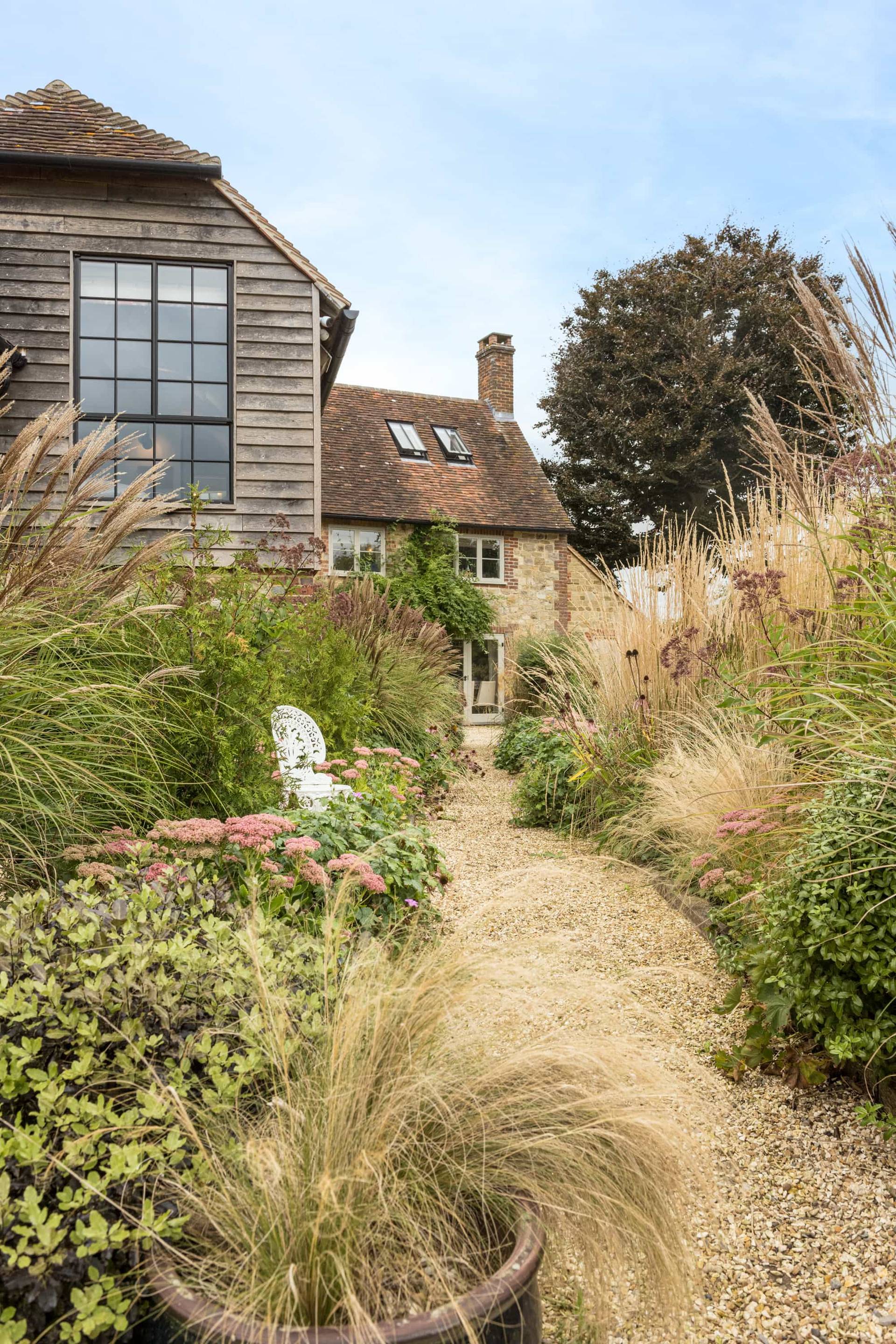 Gravel garden path lined with tall ornamental grasses and country wildflowers leading to a barn home, Love Locations GU28.