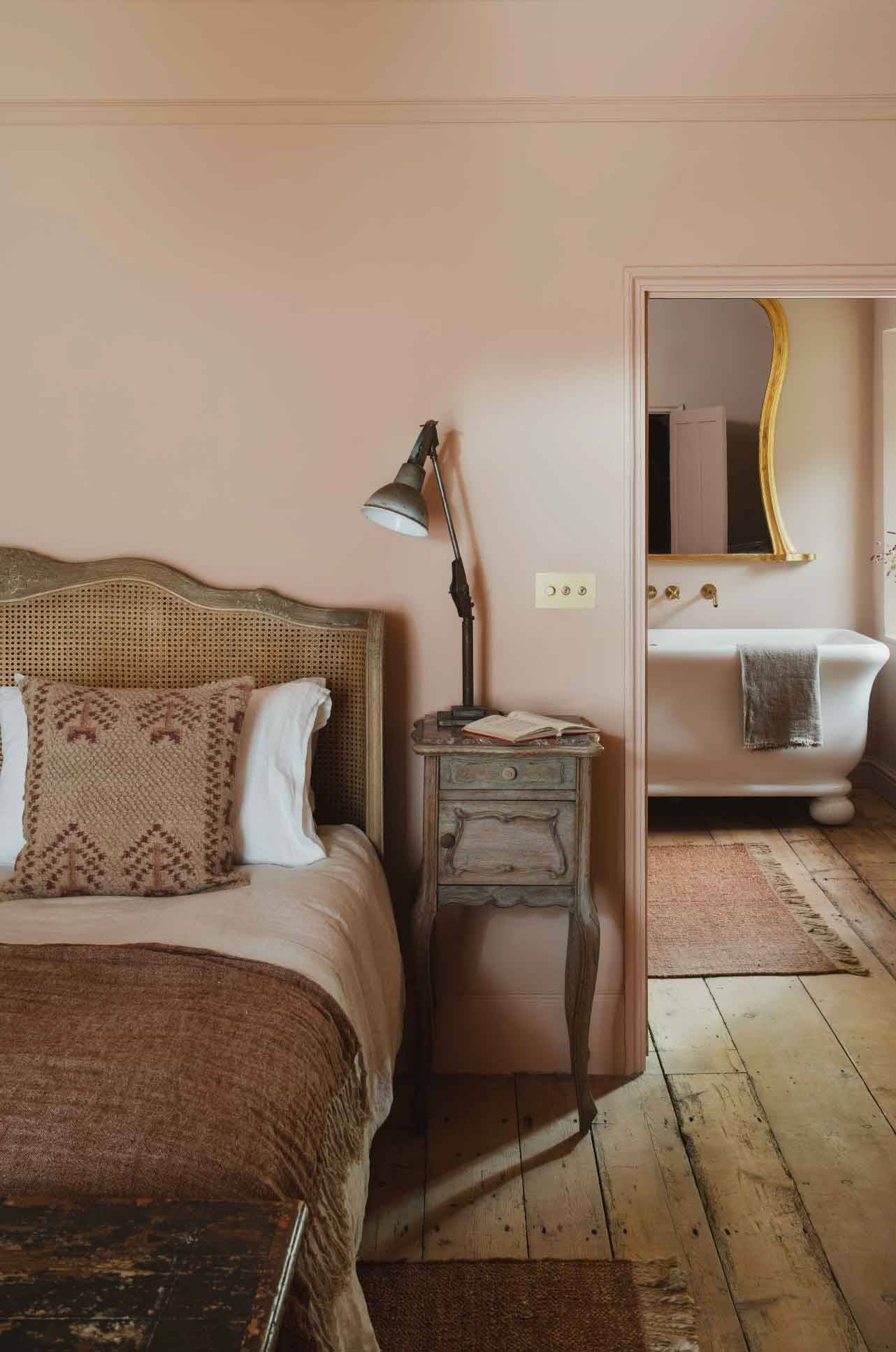Boutique bedroom corner looking through to a freestanding bathtub in a pink-toned suite via Love Locations.