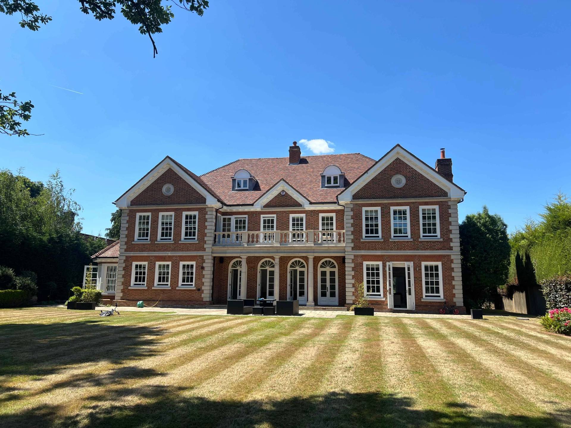 Rear exterior facade of a grand red brick Georgian-style mansion with striped manicured lawns, Love Locations BR7.