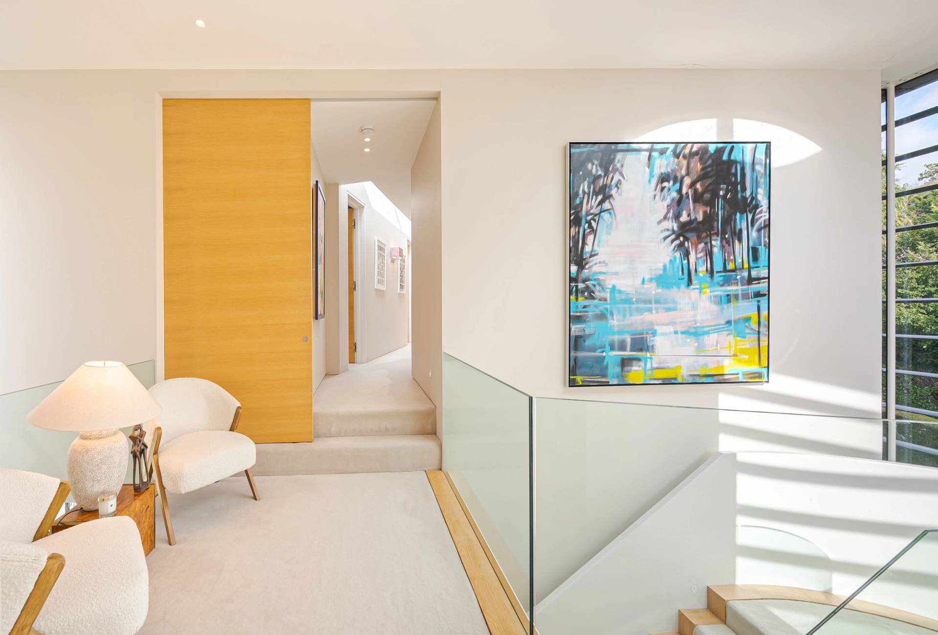 Upper gallery landing featuring sliding oak doors, glass balustrades, and modern armchair seating, Love Locations KT2.