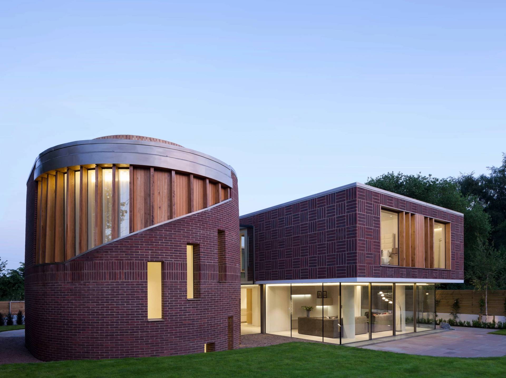 Illuminated twilight view of a modern red brick architectural home with curved facade elements, Love Locations WD7.