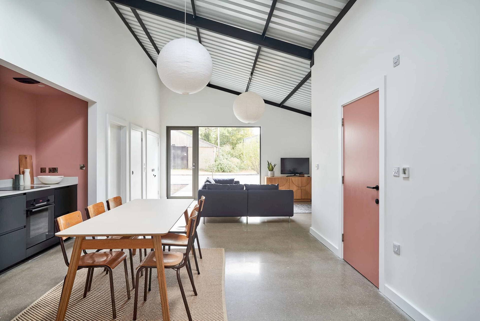 Dining and living space featuring a long wooden dining table, terracotta painted doorway, and polished concrete floors, Love Locations IP30.