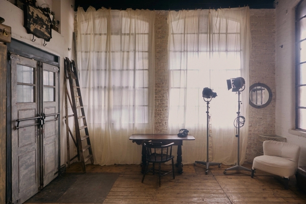 Daylight industrial photo studio location featuring large Crittall windows draped with white sheer curtains and authentic wooden floorboards, Love Locations EN5.