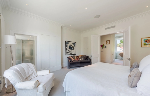Bright luxury bedroom layout featuring a large plush bed, a cozy white armchair, and deep fitted wardrobes, ideal for premium bedding lookbooks, Love Locations.