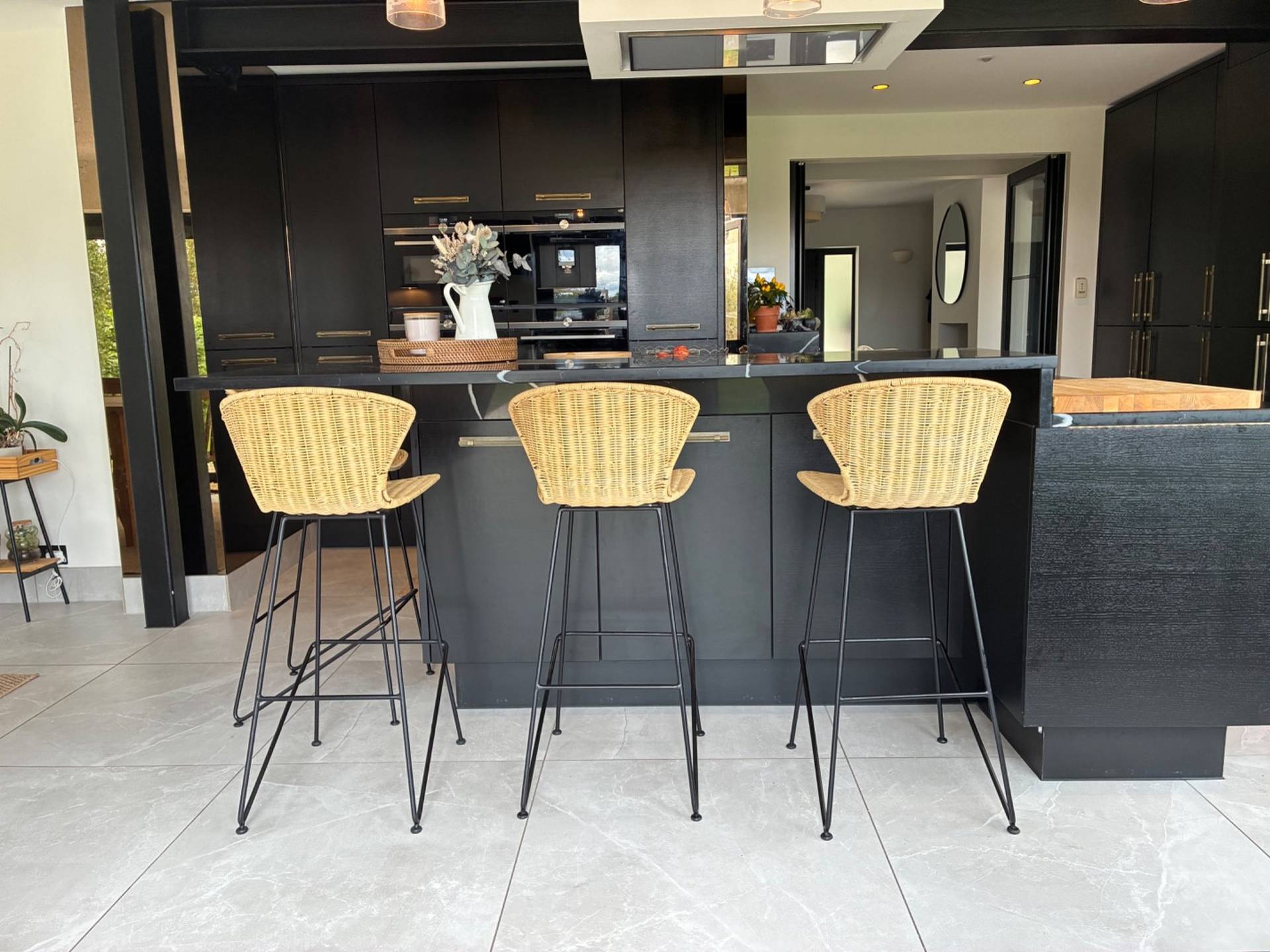 Modern kitchen breakfast bar location in Essex CM4 by Love Locations, highlighting woven counter stools set against a dark kitchen island backdrop.