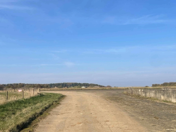 Open rural roadway and farm access track connecting historic airfield and agricultural spaces, Love Locations NN17.