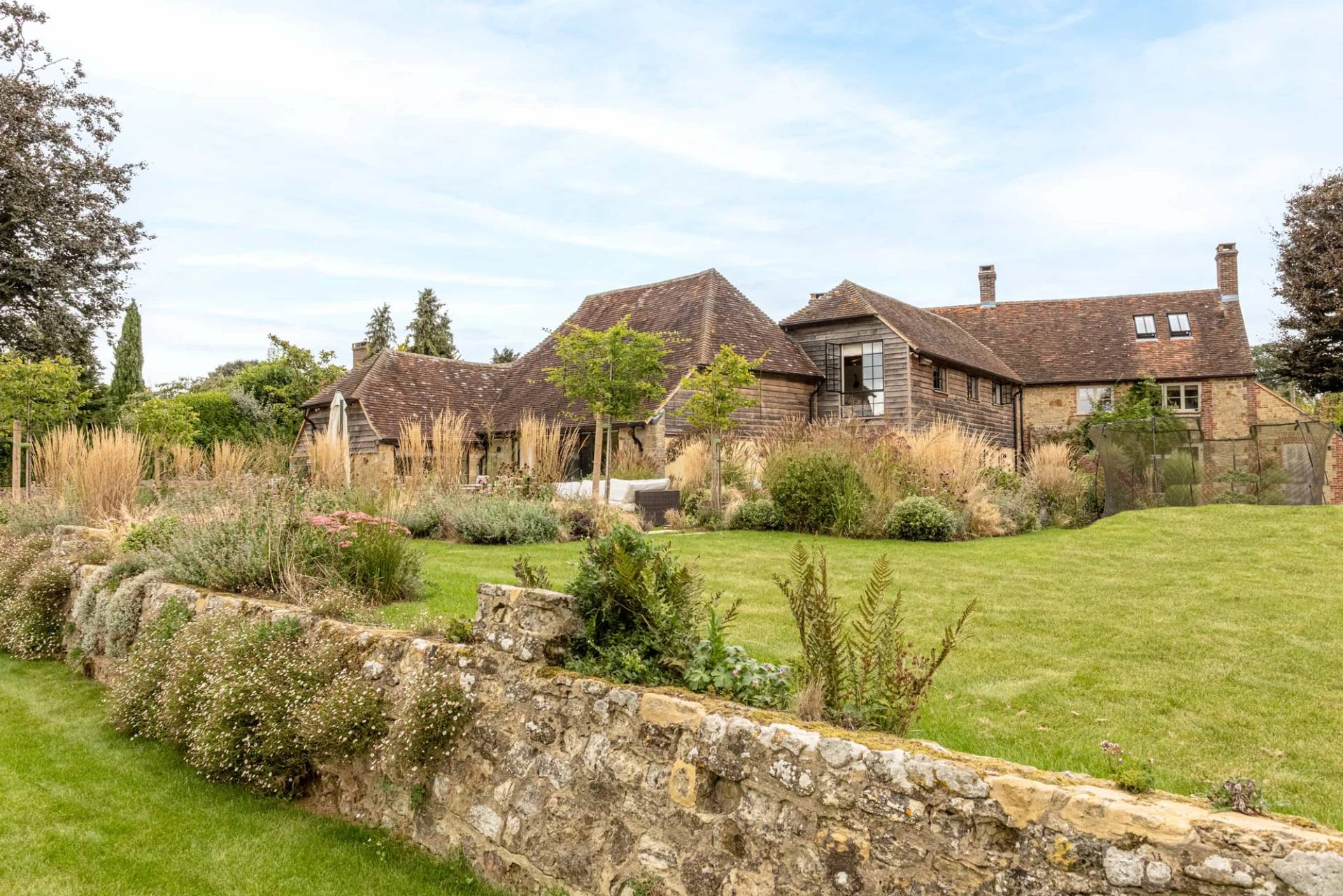 Old stone garden wall bordering a manicured green lawn in a West Sussex country estate, Love Locations GU28.