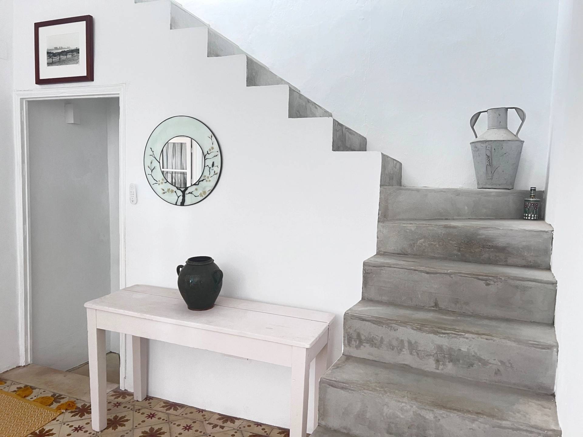 Bright white hallway and stone staircase in a traditional Spanish townhouse shoot location in Jimena de la Frontera via Love Locations, featuring a console table and round mirror.
