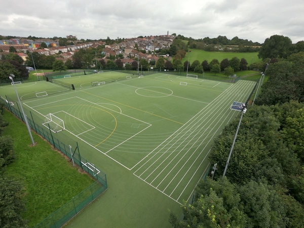 Love Locations campus drone photography Bristol BS7: Elevated perspective showing extensive artificial turf sports pitches, running track lanes, and neighboring residential areas, great for commercial video.