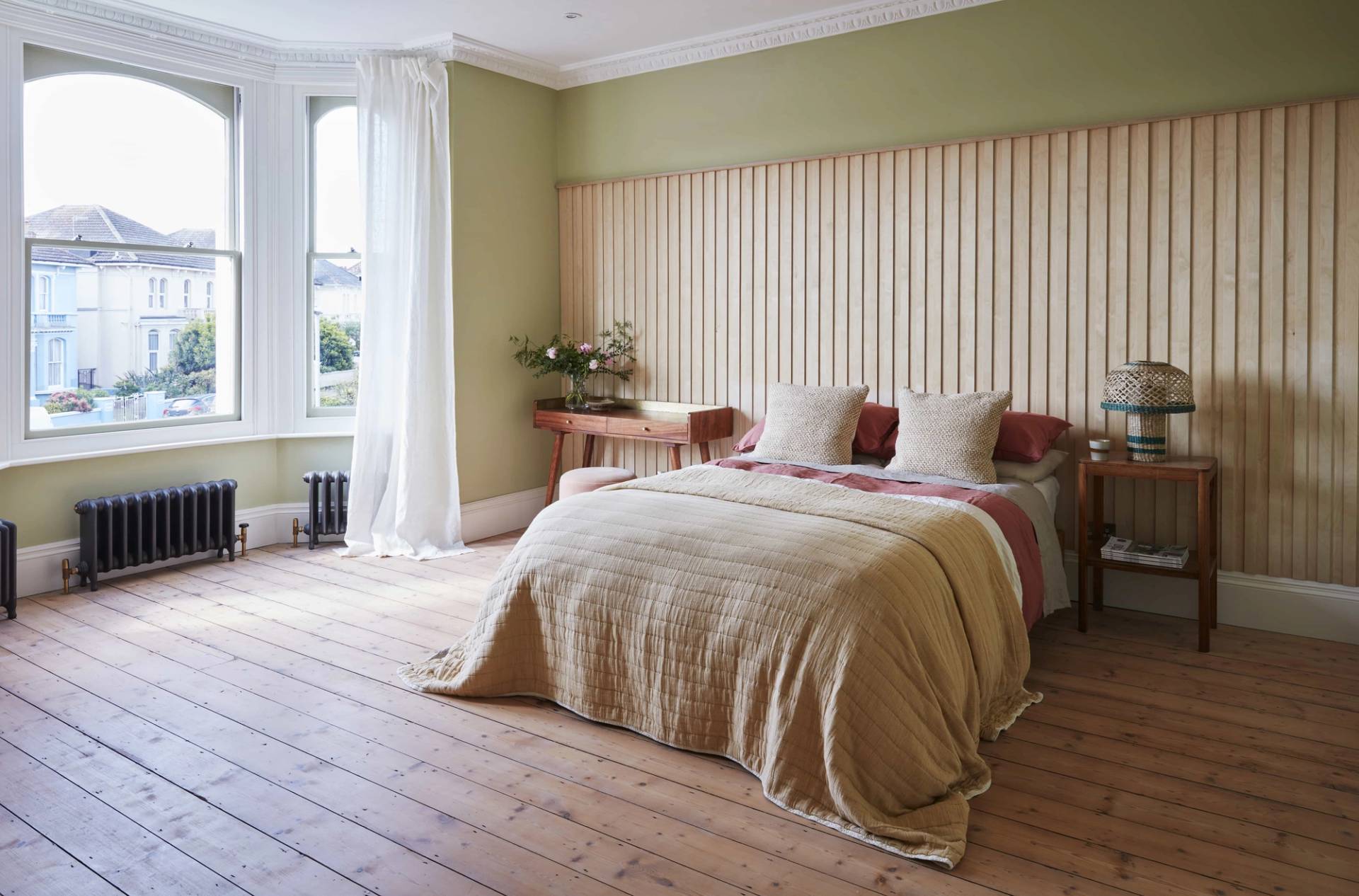 Master bedroom with a slatted wooden headboard wall, green accent panelling, and sash window views, perfect for bedding ads, Love Locations.