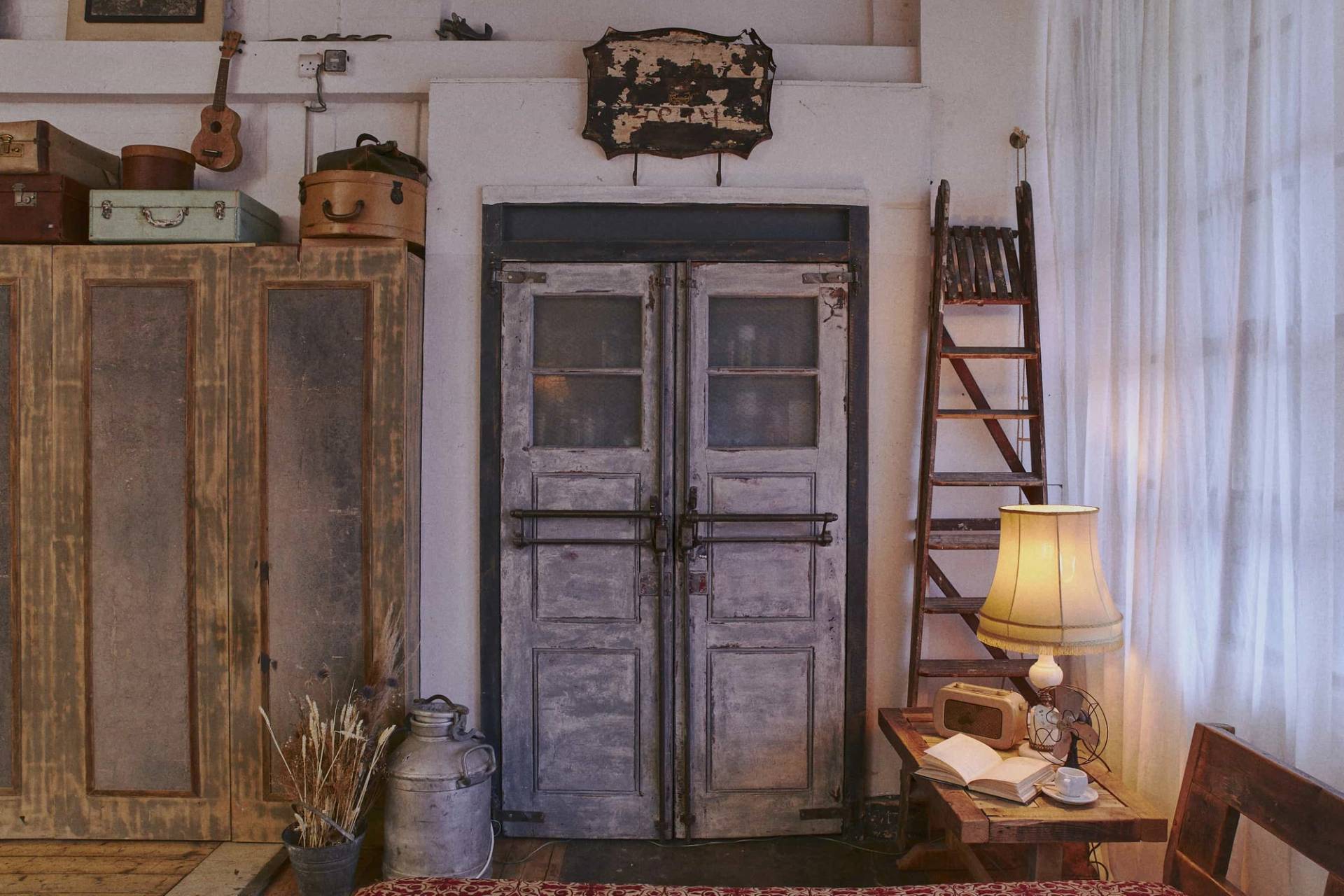 Distressed double factory entrance doors framed by a wooden ladder, vintage milk churns, and a floor lamp, Love Locations EN5.