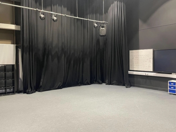 Love Locations theatre rehearsal location Reading: Empty blacked-out drama studio with track lighting and a white evaluation board, tailored for experimental music videos and actor interview setups.