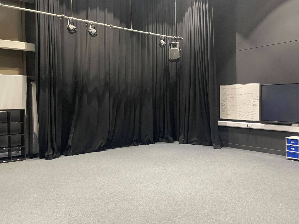 Love Locations theatre rehearsal location Reading: Empty blacked-out drama studio with track lighting and a white evaluation board, tailored for experimental music videos and actor interview setups.