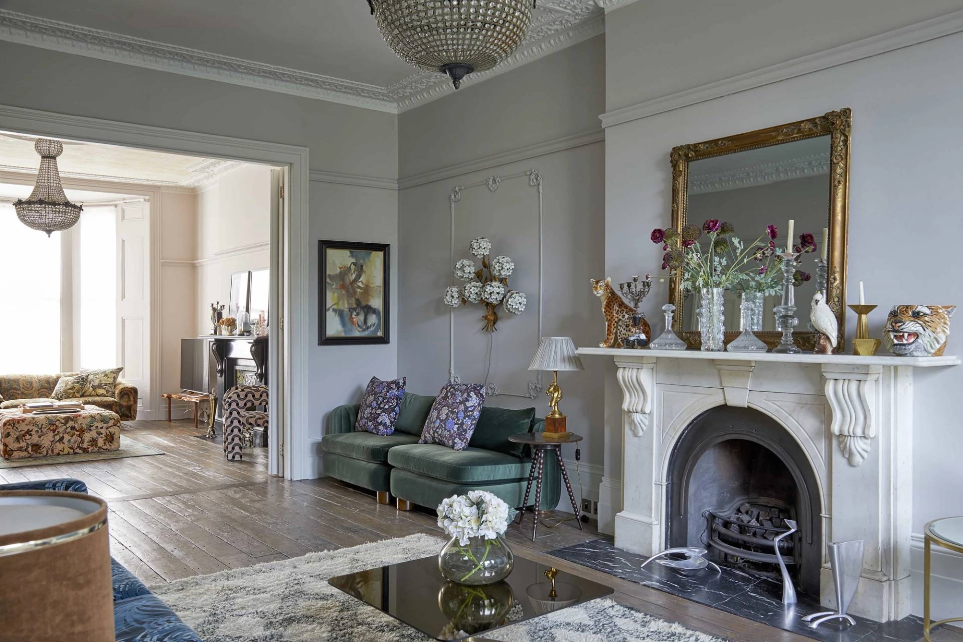 Wide perspective of a double reception room with twin marble fireplaces, crystal chandeliers, and blue patterned sofa, Love Locations N16.