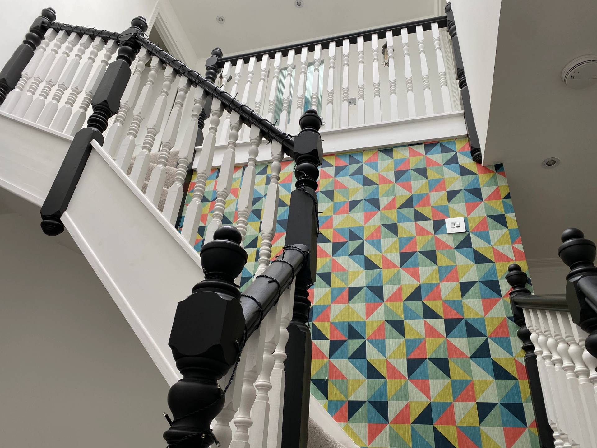 Staircase landing view looking down on geometric multi-colored floor tiles and black banisters, Love Locations Ealing Common.