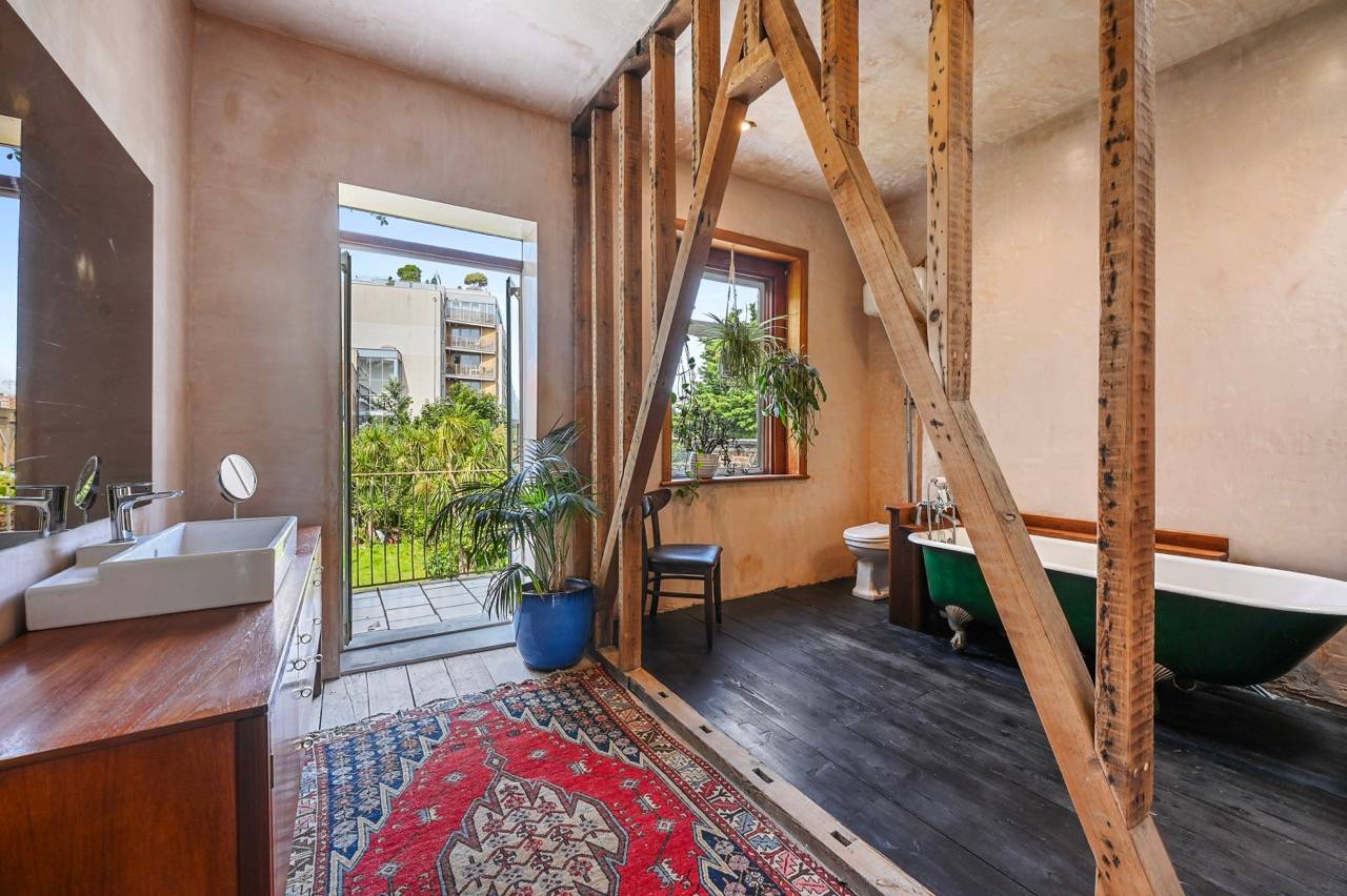 Master bathroom transition view with exposed timber studwork, red patterned rug, and patio door access, Love Locations.
