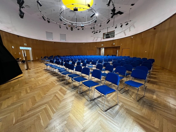 Love Locations lecture theatre shoot location SE2: Unique circular auditorium with wood panelled walls and rows of blue chairs under a central studio lighting rig, perfect for cinema crowd scenes.