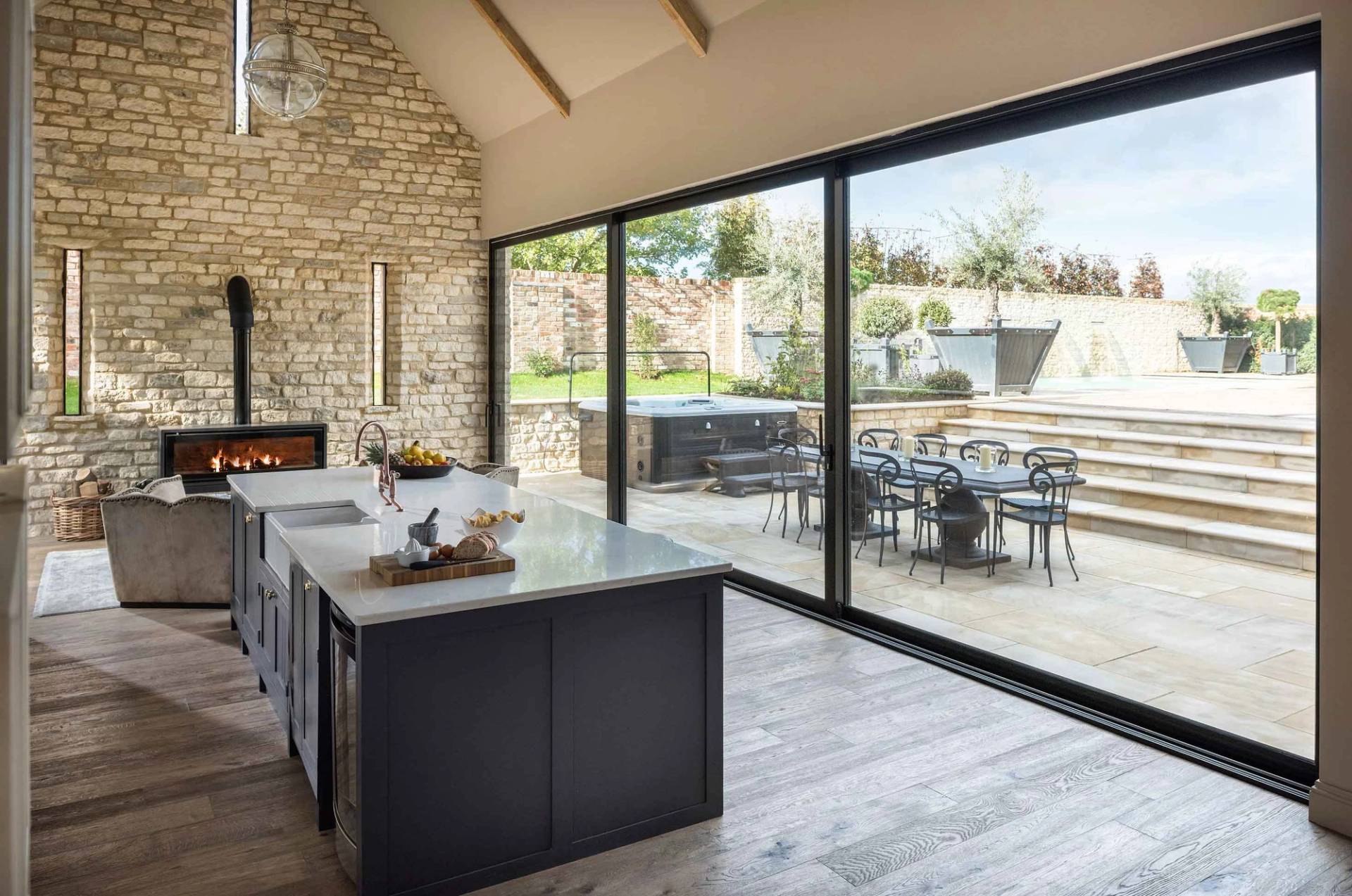 Light-filled kitchen shoot space in Cheltenham Gloucestershire by Love Locations, showcasing exposed 18th-century stone walls, high timber ceilings, and bi-fold doors opening to an outdoor patio.