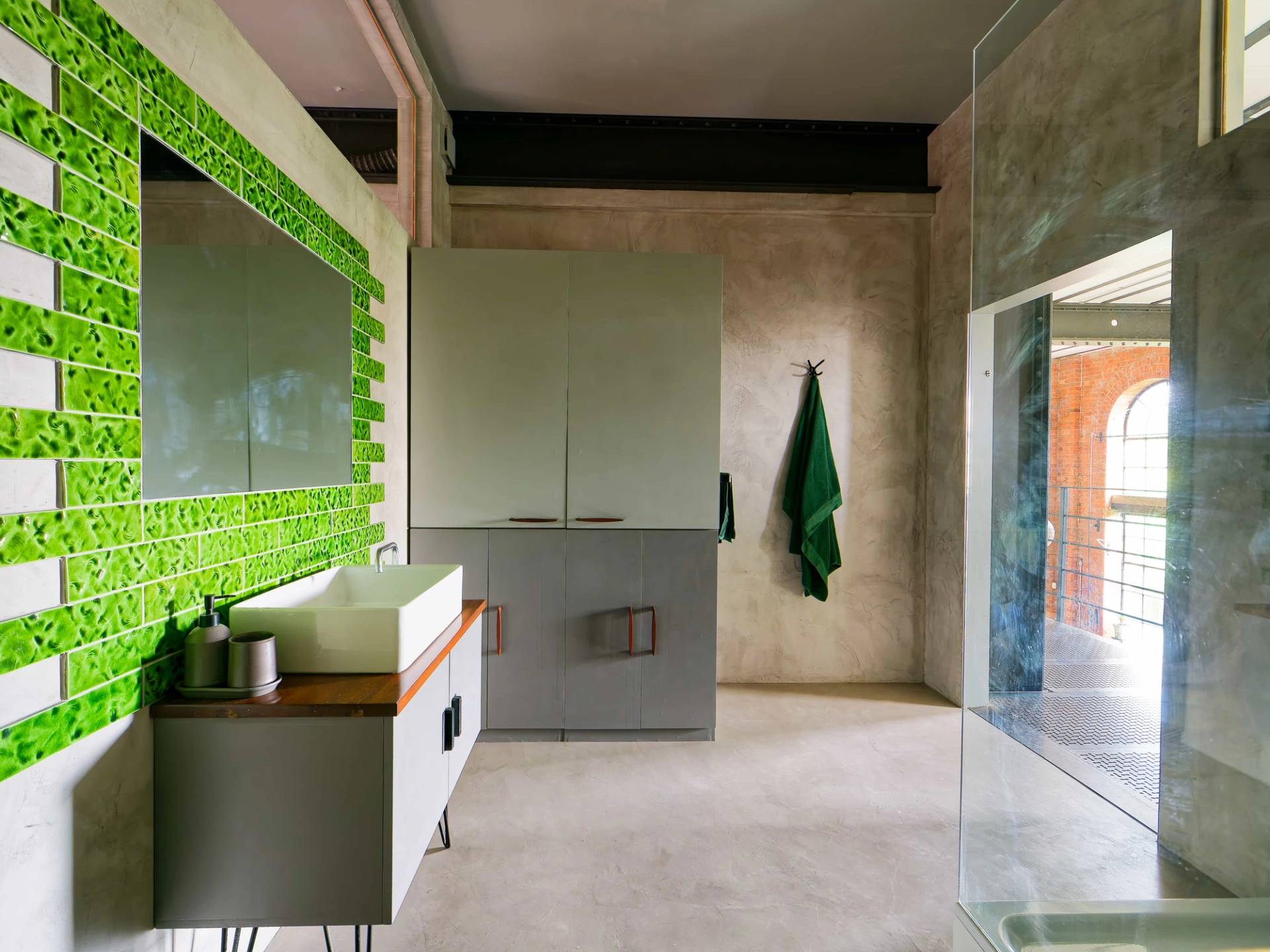 Micro-cement bathroom console with sage green storage cabinet, white washbasin, and glass shower enclosure, Love Locations.