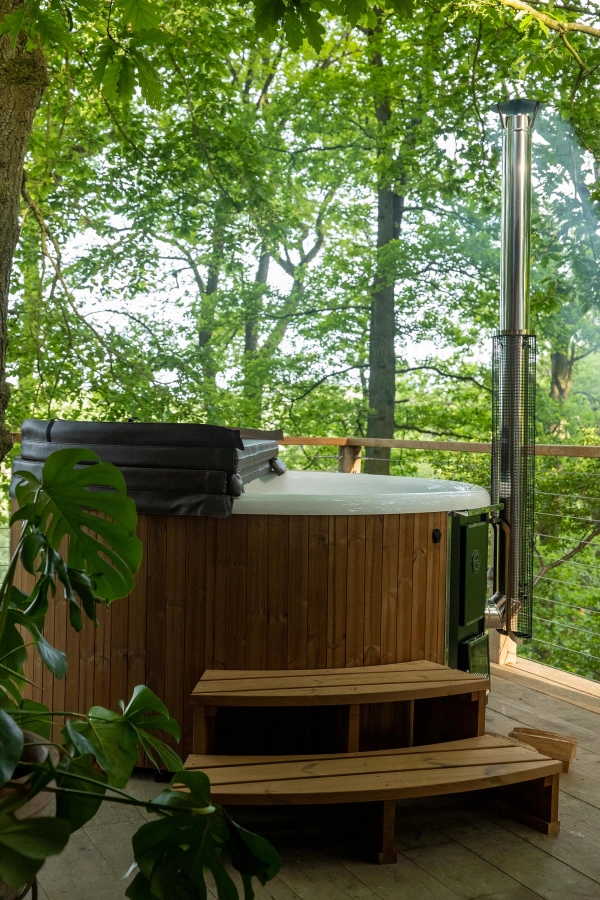 Close-up shot of a wood-fired outdoor soaking tub on a secluded forest balcony platform, a unique setting for wellness brand advertising via Love Locations.