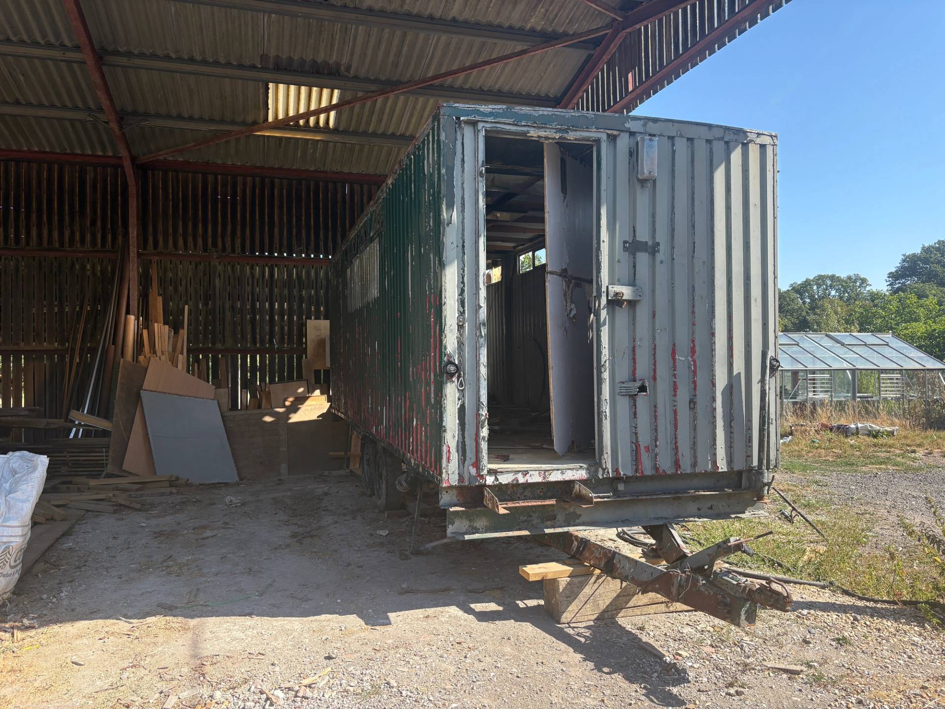 Weathered metal shipping container box trailer parked inside a covered steel-frame farm barn, Love Locations BN8.