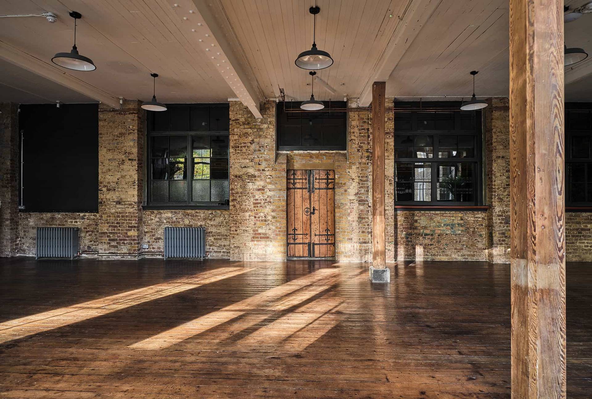 Sunlit industrial warehouse hall with wooden double doors and overhead pendant lights, Love Locations.