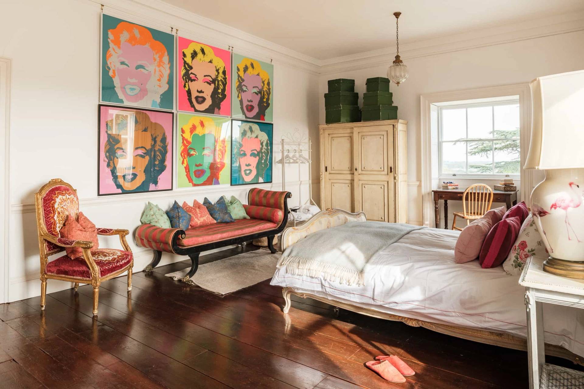 Eclectic bedroom interior featuring vibrant pop-art wall prints, wooden floorboards, and bright daybed seating, Love Locations RG42.