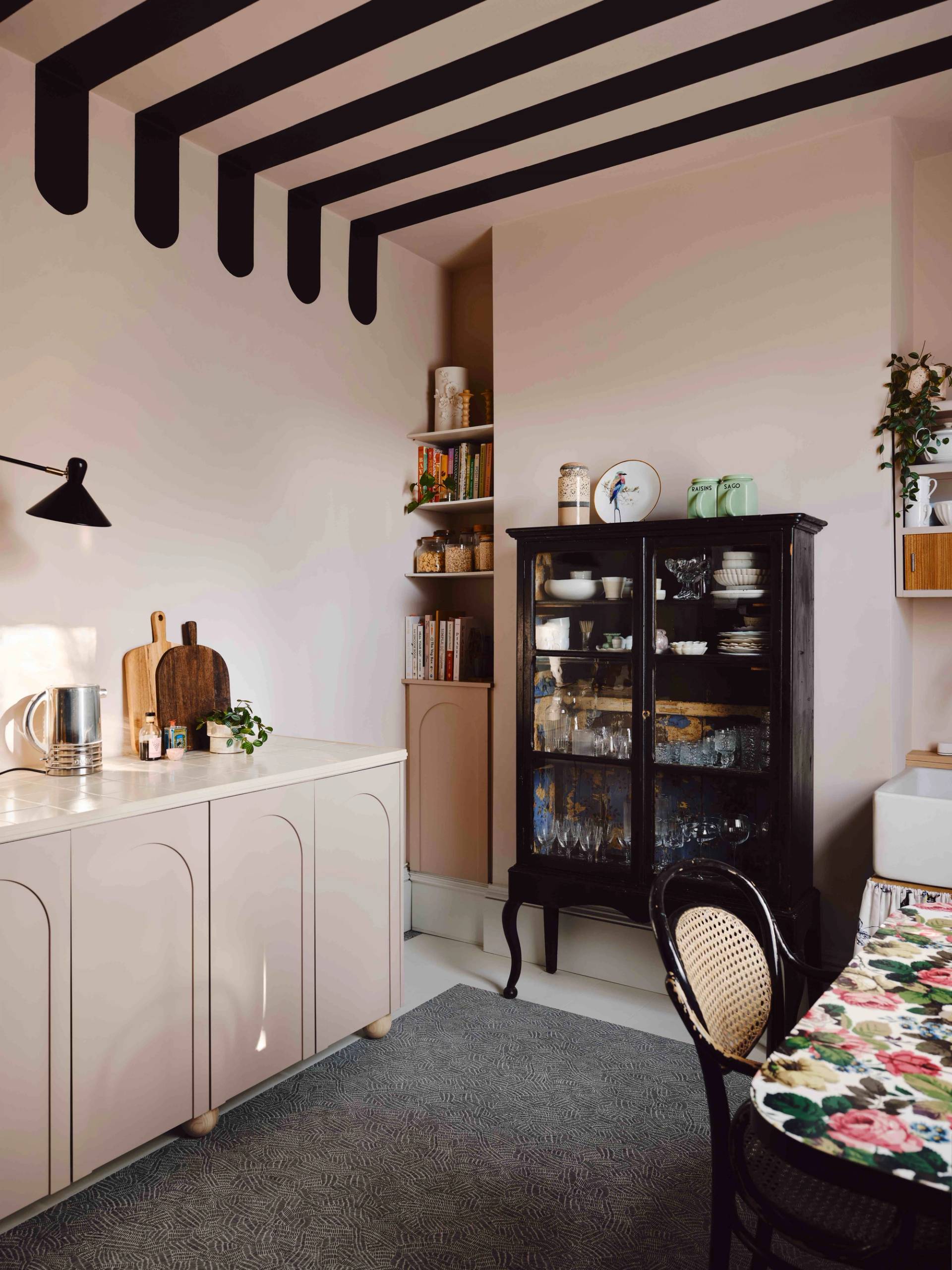 Pink painted kitchen location featuring a dark glass-front display cabinet, pink cabinetry, and open wall shelves, Love Locations CR0.