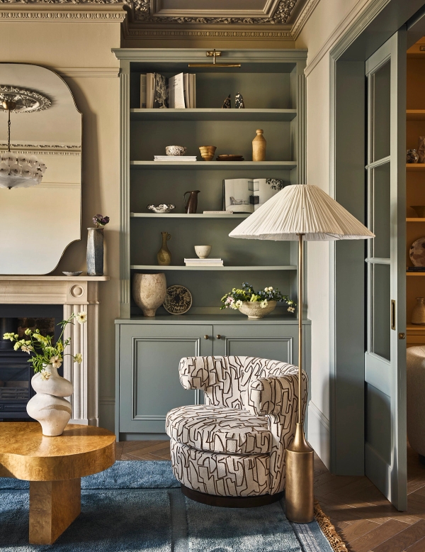Built-in grey painted alcove shelving set beside an ornate white fireplace mantel and patterned armchair, Love Locations SE21.