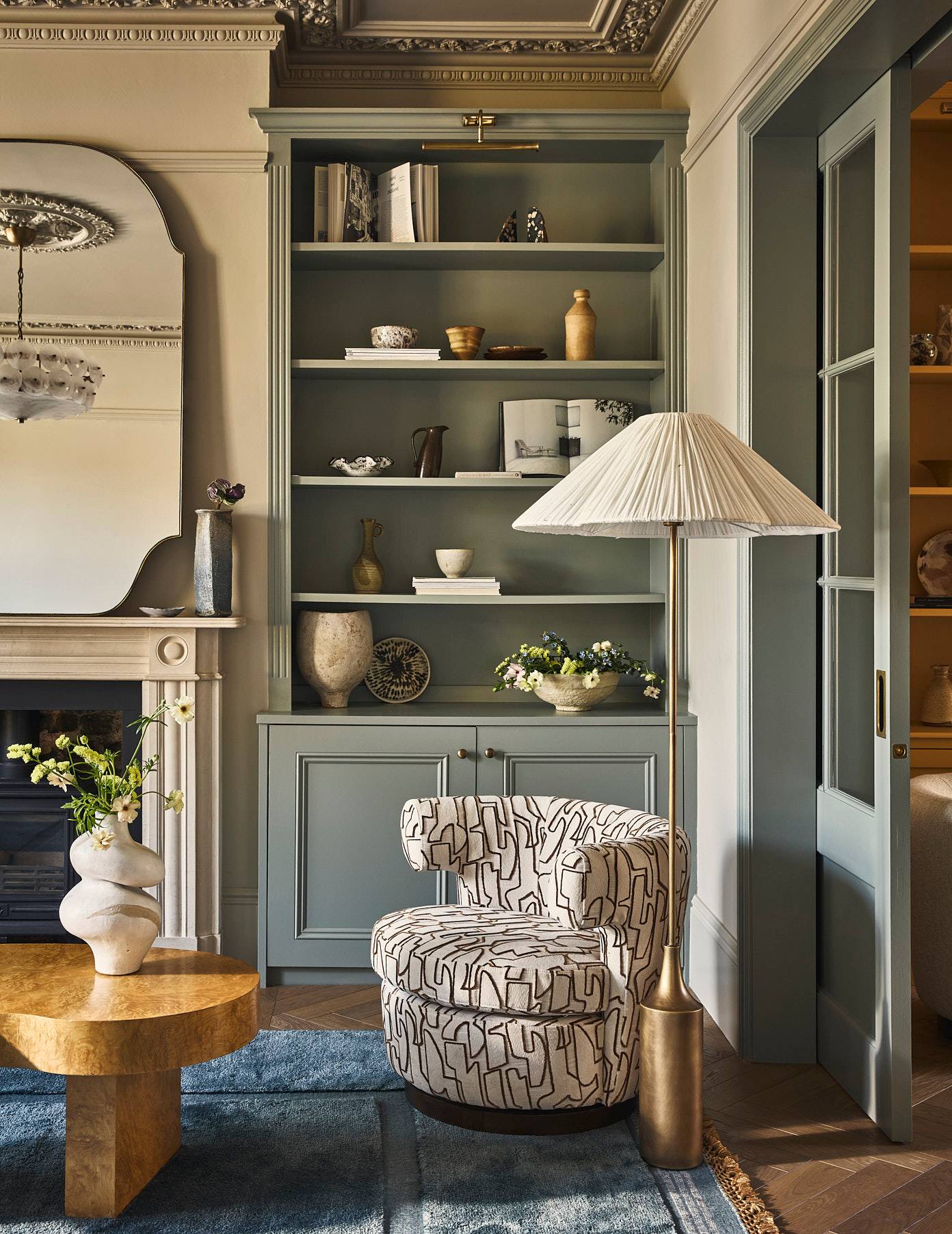 Built-in grey painted alcove shelving set beside an ornate white fireplace mantel and patterned armchair, Love Locations SE21.