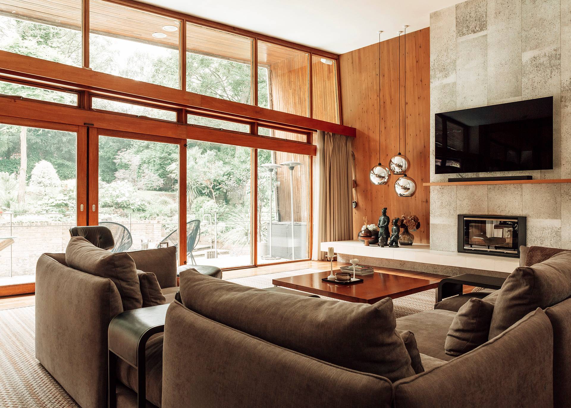 Mid-century modern lounge space with expansive glass sliding doors looking out onto a lush green garden setting, Love Locations.