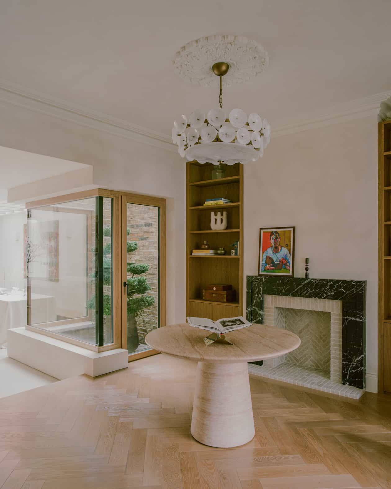 Light-filled reception room featuring green marble fireplace hearth, round dining table, oak bookcases, and parquet flooring in SW4, Love Locations.