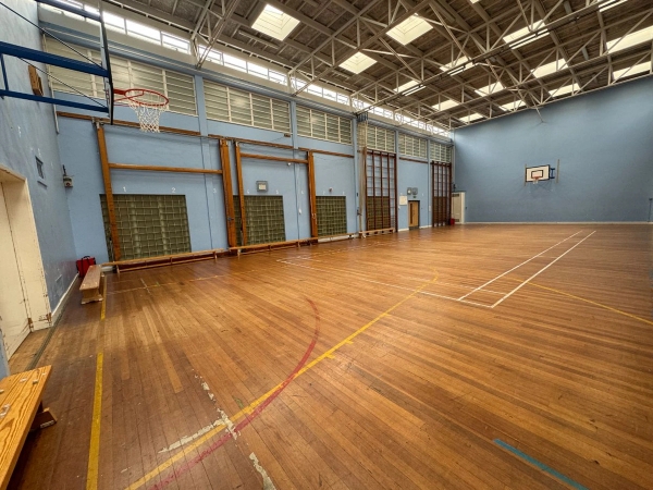 Love Locations traditional school gym shoot location Cockfosters: Classic sports hall featuring wood-panelled walls, wall bars, a basketball hoop, and polished floor court markings, great for physical education scenes.