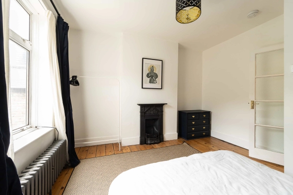Love Locations minimalist bedroom shoot space Forest Gate: Bright neutral room with a period cast iron bedroom fireplace and dark chest of drawers, excellent for clothing lookbooks and film sets.