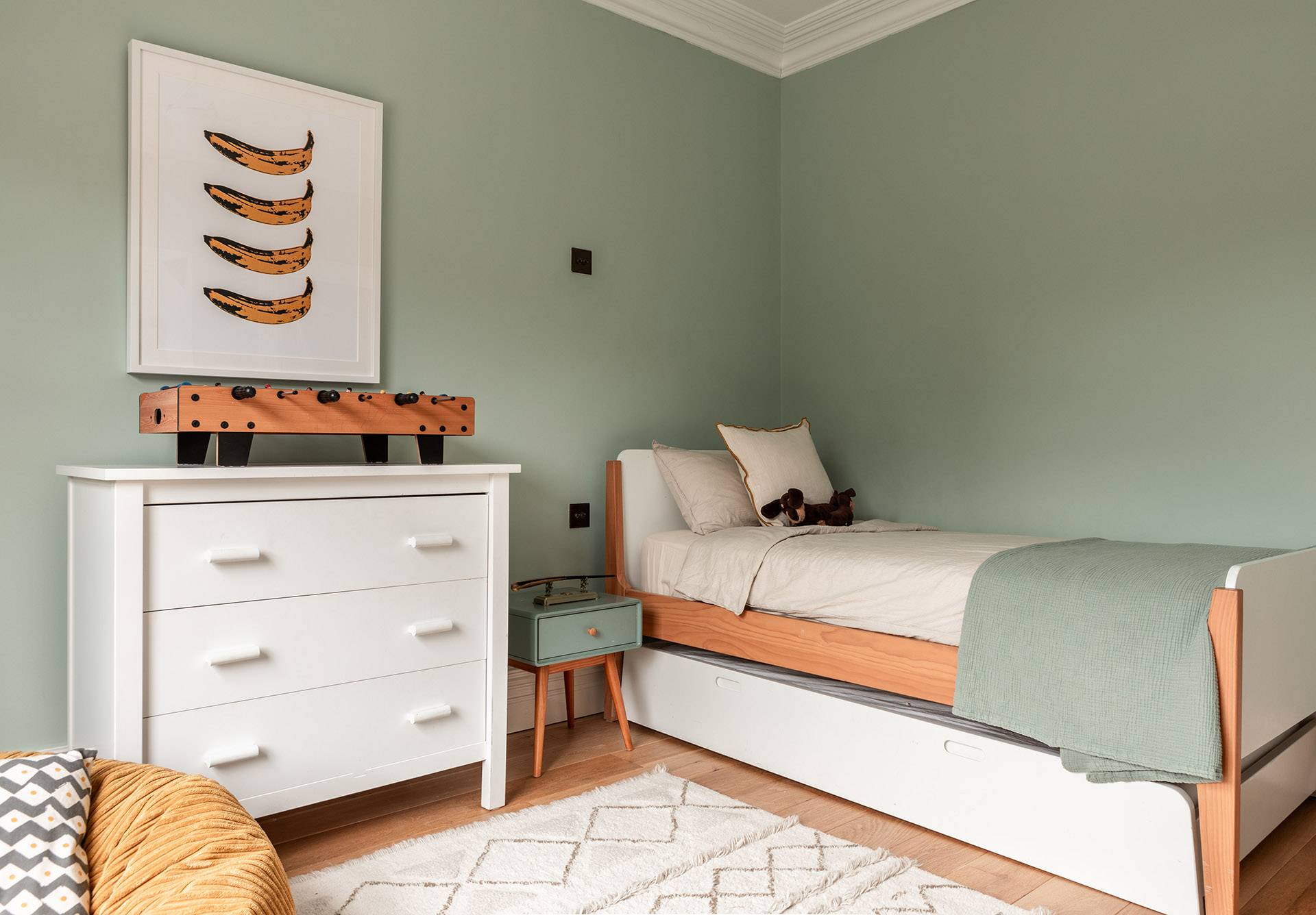 Sage green children's bedroom featuring white wooden furniture, single bed, and playful decor, ideal for kids apparel ads, Love Locations.