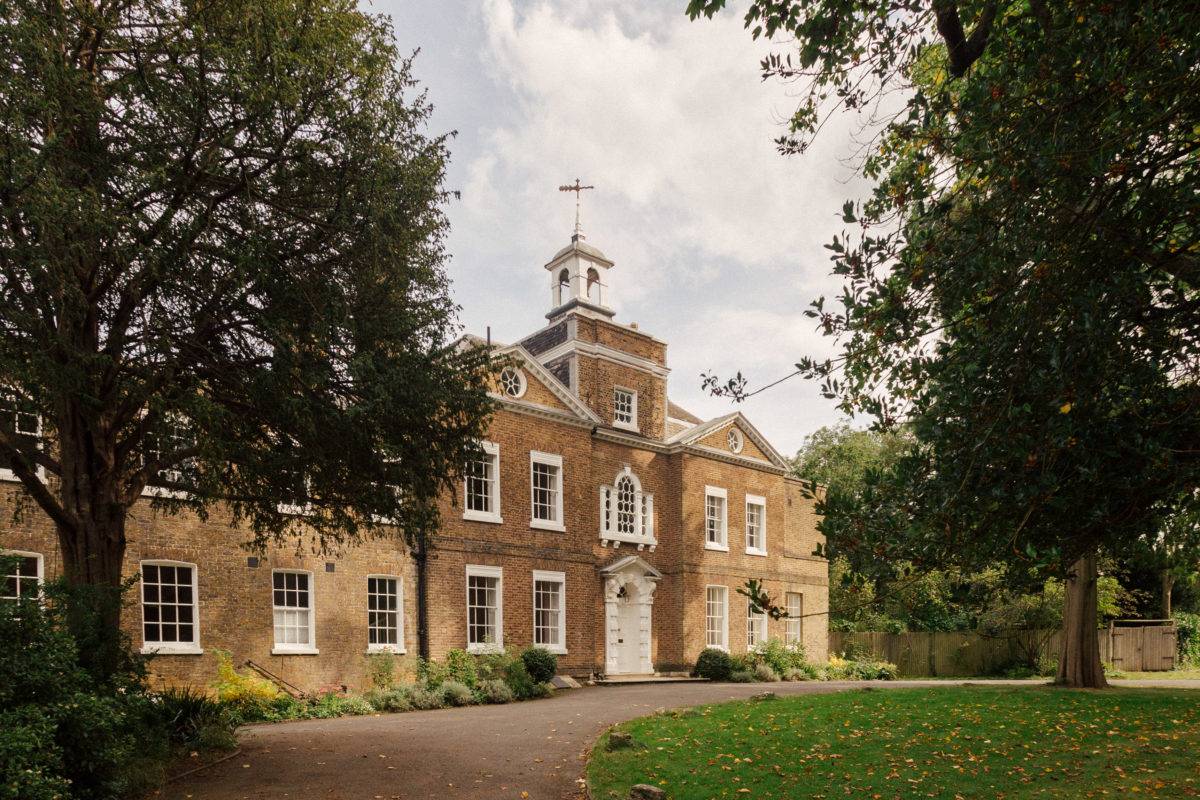 Full front exterior view of a stately Georgian manor house with a portico entrance and cupola, Love Locations.
