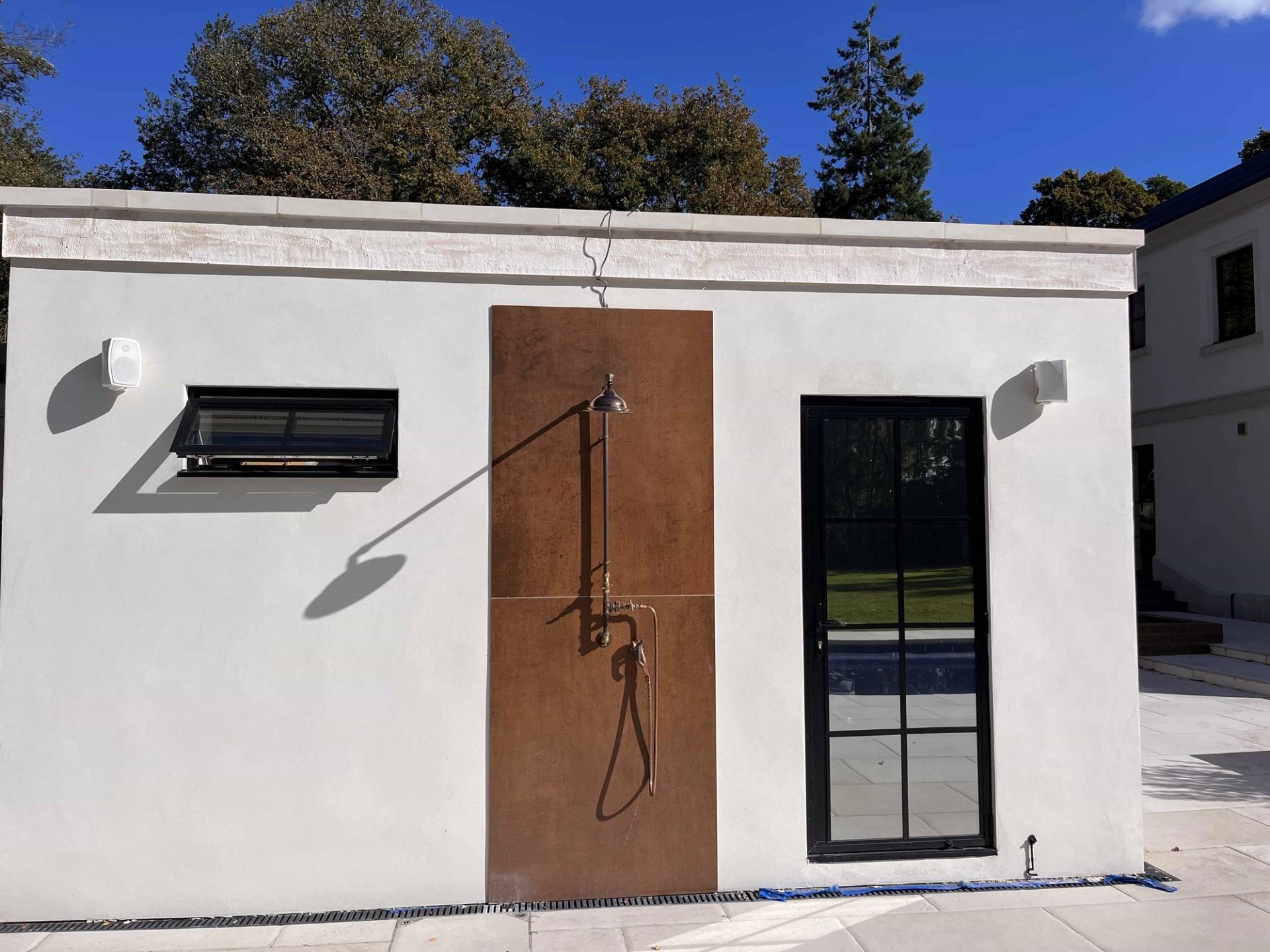 Outdoor shower feature wall with rusty steel panelling and black fixtures set on an exterior rendered wall, Love Locations GU3.