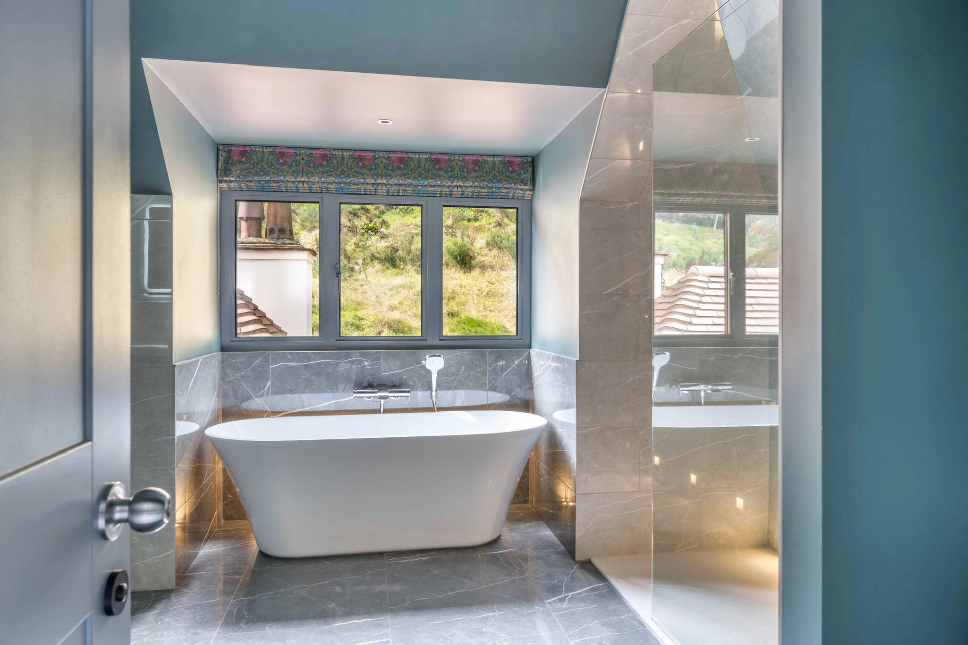 Luxury master bathroom featuring a white freestanding soaking tub set before garden windows and marble tile walls, perfect for skincare commercials, Love Locations GU27.